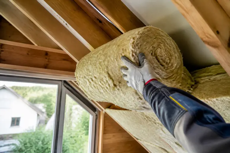 Professionelle Handwerker verlegen Dämmmaterialien auf der obersten Geschossdecke eines Wohnhauses, um Energieverluste zu reduzieren.
