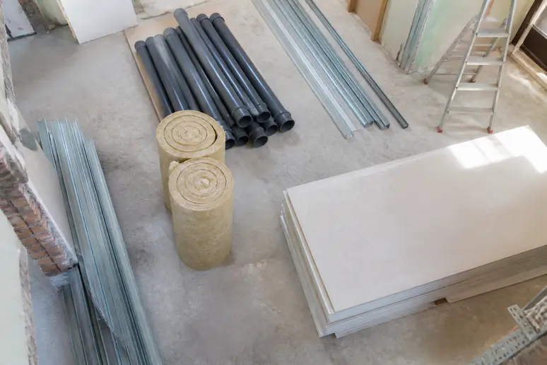 Baumaterialien wie Rohre, Dämmung und Gipskartonplatten liegen bereit für eine Kernsanierung eines Hauses.