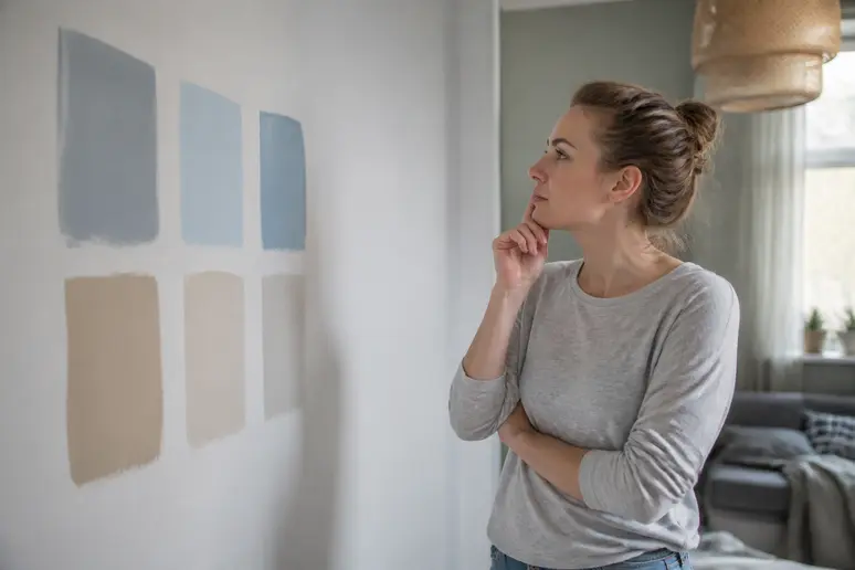 Eine junge Frau wählt helle Wandfarben für ein Wohnzimmer mit wenig Tageslicht aus, um den Raum optisch zu vergrößern.