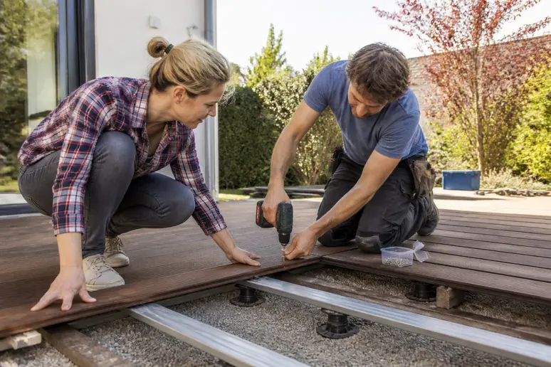 Ein Paar verlegt gemeinsam Terrassendielen auf einer vorbereiteten Unterkonstruktion im Garten eines Hauses.