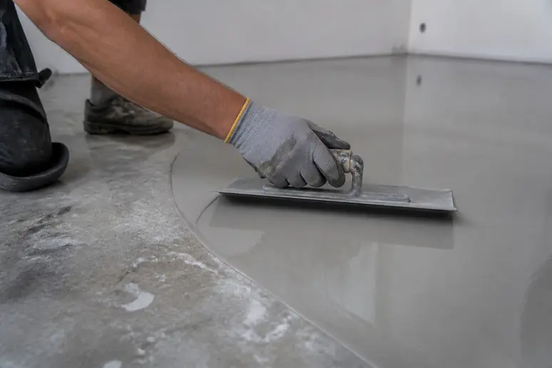 Handwerker glättet Ausgleichsmasse auf Estrich mit Glättekelle für ebenen Untergrund.