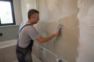 Handwerker klebt Fliesen sorgfältig auf vorbereiteten Putz im Badezimmer mit Spezialwerkzeug.