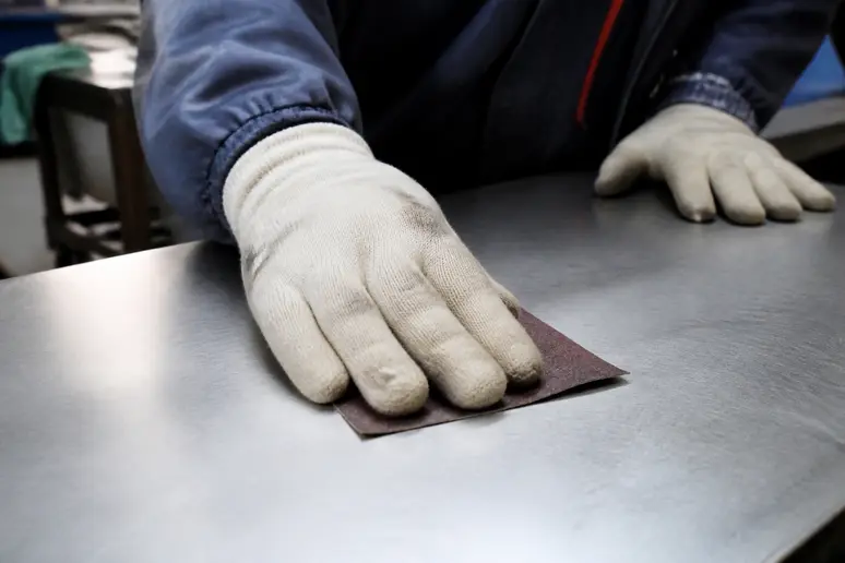 Maler schleift Edelstahlfläche mit Schleifpapier für bessere Grundhaftung an.
