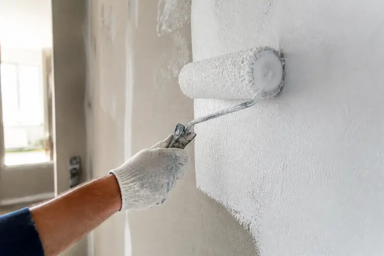 Maler trägt weiße Grundierung auf Wand auf, um das Durchscheinen der Goldtapete zu verhindern.