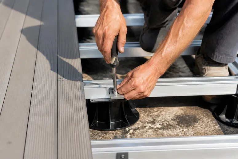 Hände eines Handwerkers montieren Aluminiumträger für eine WPC-Terrassenunterkonstruktion, Detailansicht.